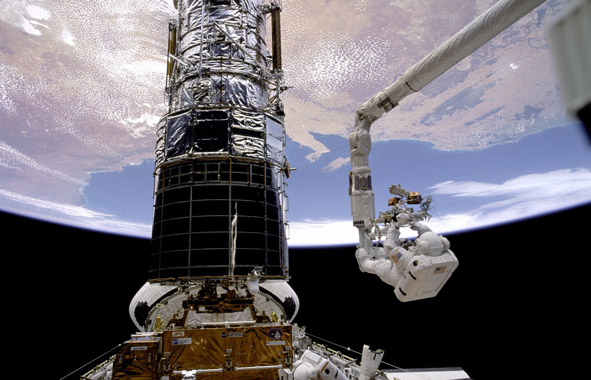 Astronaut outside shuttle working on Hubble telescope with Earth in the background