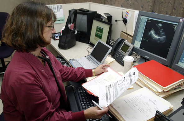 A doctor goes over paper records in an examine room at the Indiana Heart Hospital in Indianapolis.