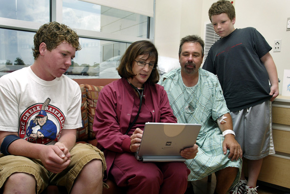 A doctor explains a patient's condition to him and his family using an eletronic medical record on a laptop.