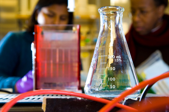 beaker in a lab with two scientists working the background